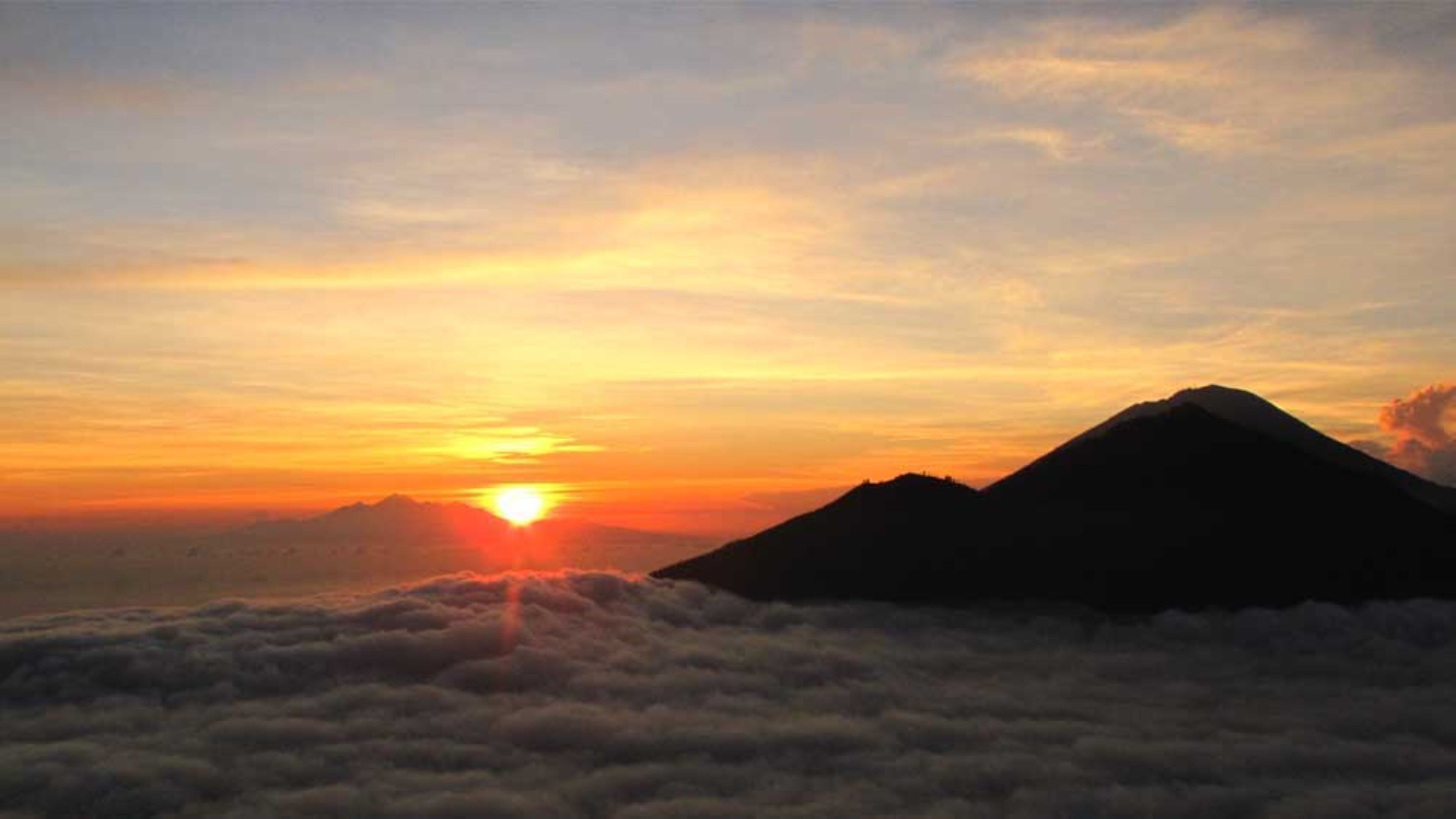 A mountain landscape at sunrise with clouds below.