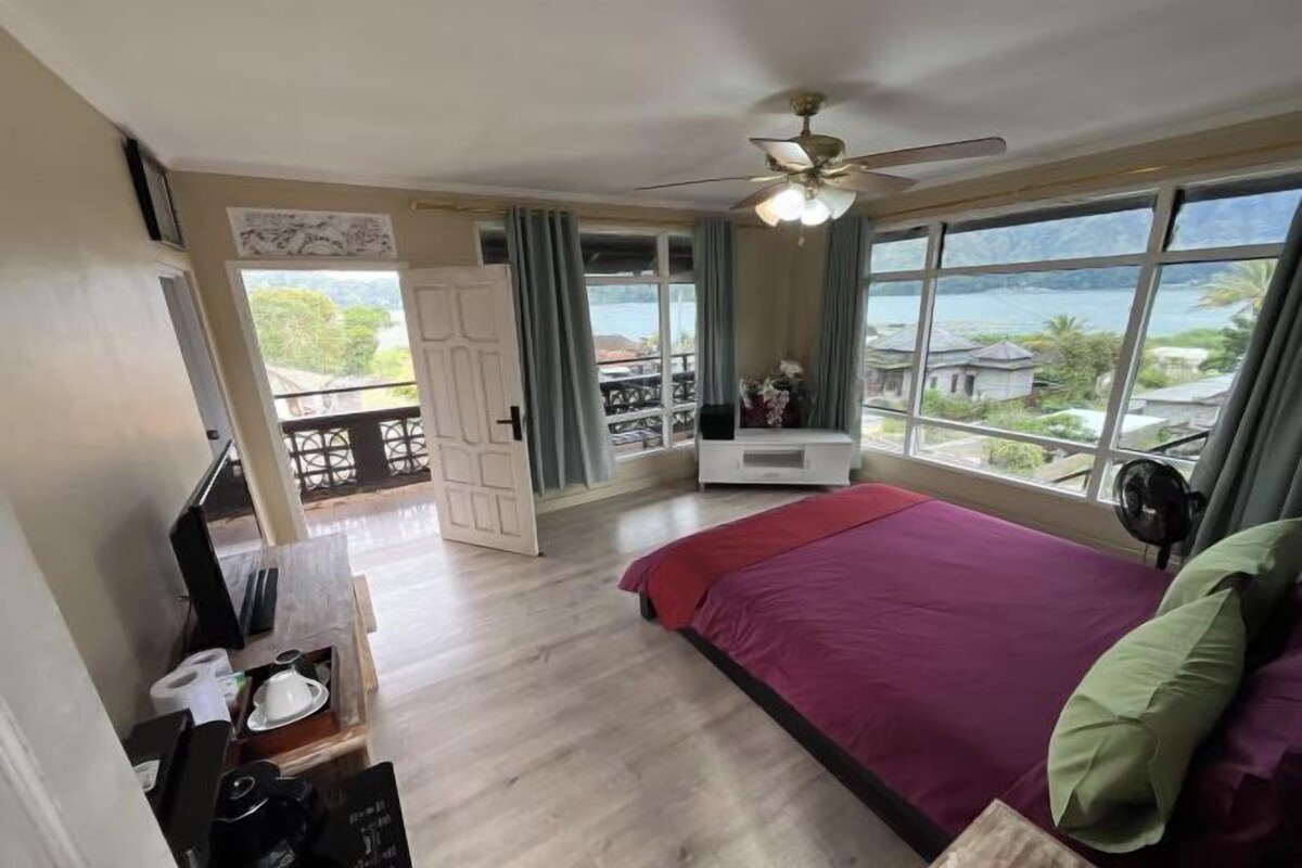 Une chambre avec un lit, un ventilateur de plafond, une fenêtre donnant sur un beau paysage et un balcon.