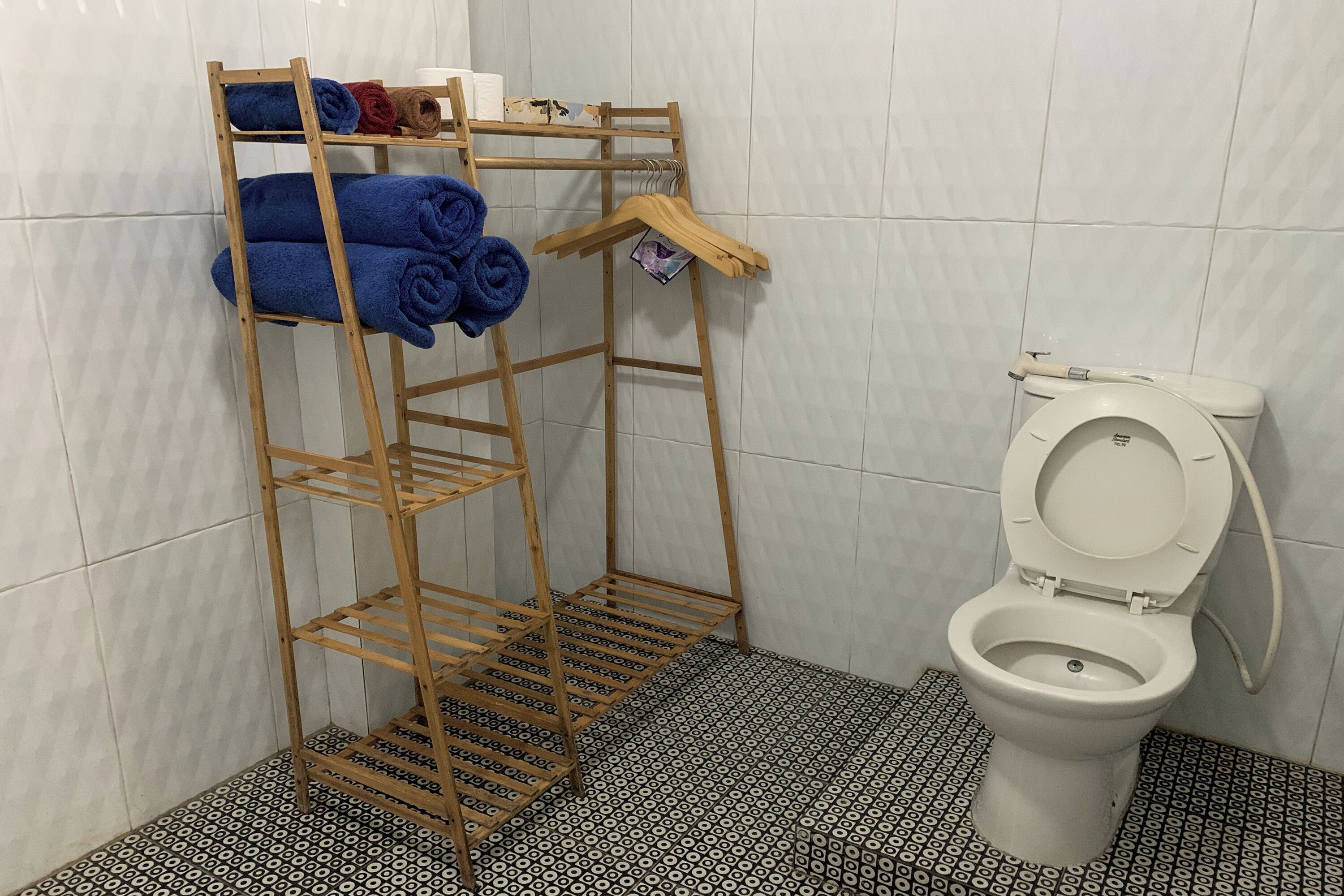 Een badkamer met een toilet, een houten handdoekhouder met handdoeken en vloertegels met een patroon.