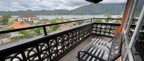 A balcony with a view of a lake and mountains, a metal railing, and a bench.