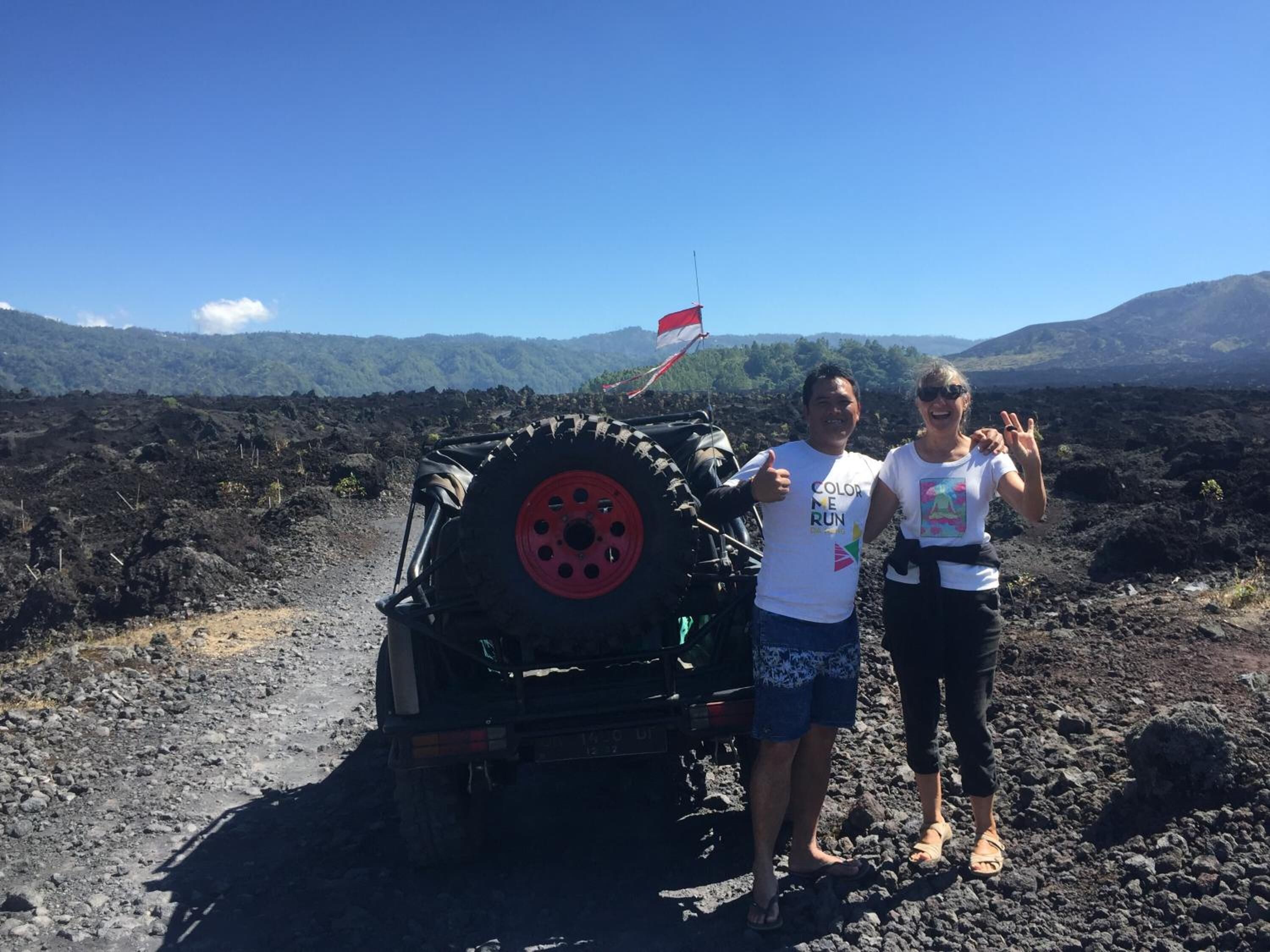 A vehicle with a red wheel and a flag on its back, parked on a rocky terrain with mountains in the background.