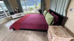 Une chambre avec un grand lit, une table de chevet en bois, un meuble TV blanc et une vue sur la mer et les montagnes.