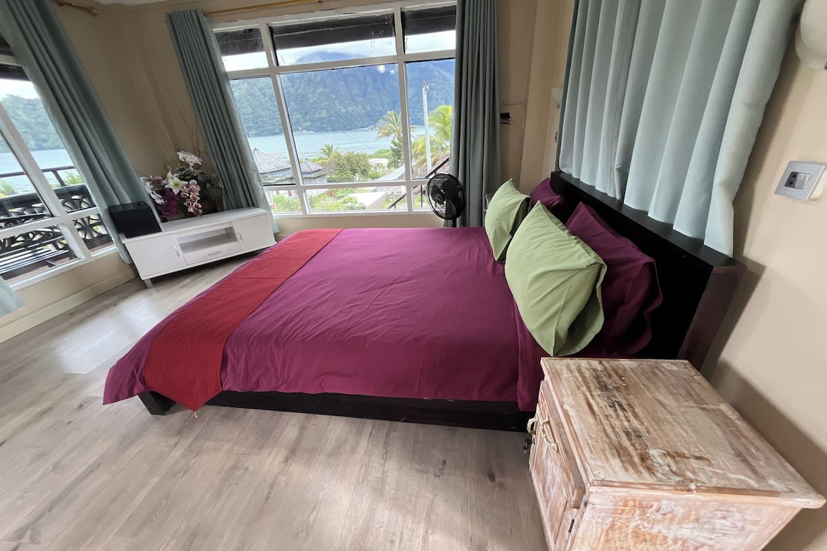 Un dormitorio con una cama grande, una mesita de noche de madera, un mueble blanco para televisor y vistas al mar y a las montañas.