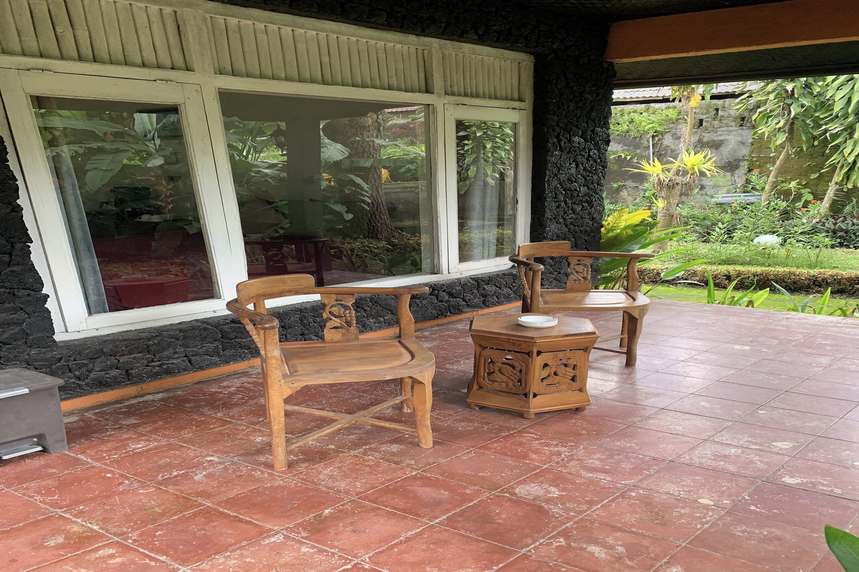 Un patio con muebles de madera, una pared de piedra y grandes ventanales que dan a un jardín.