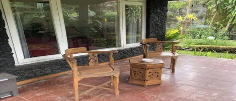 Un patio con muebles de madera, una pared de piedra y grandes ventanales que dan a un jardín.