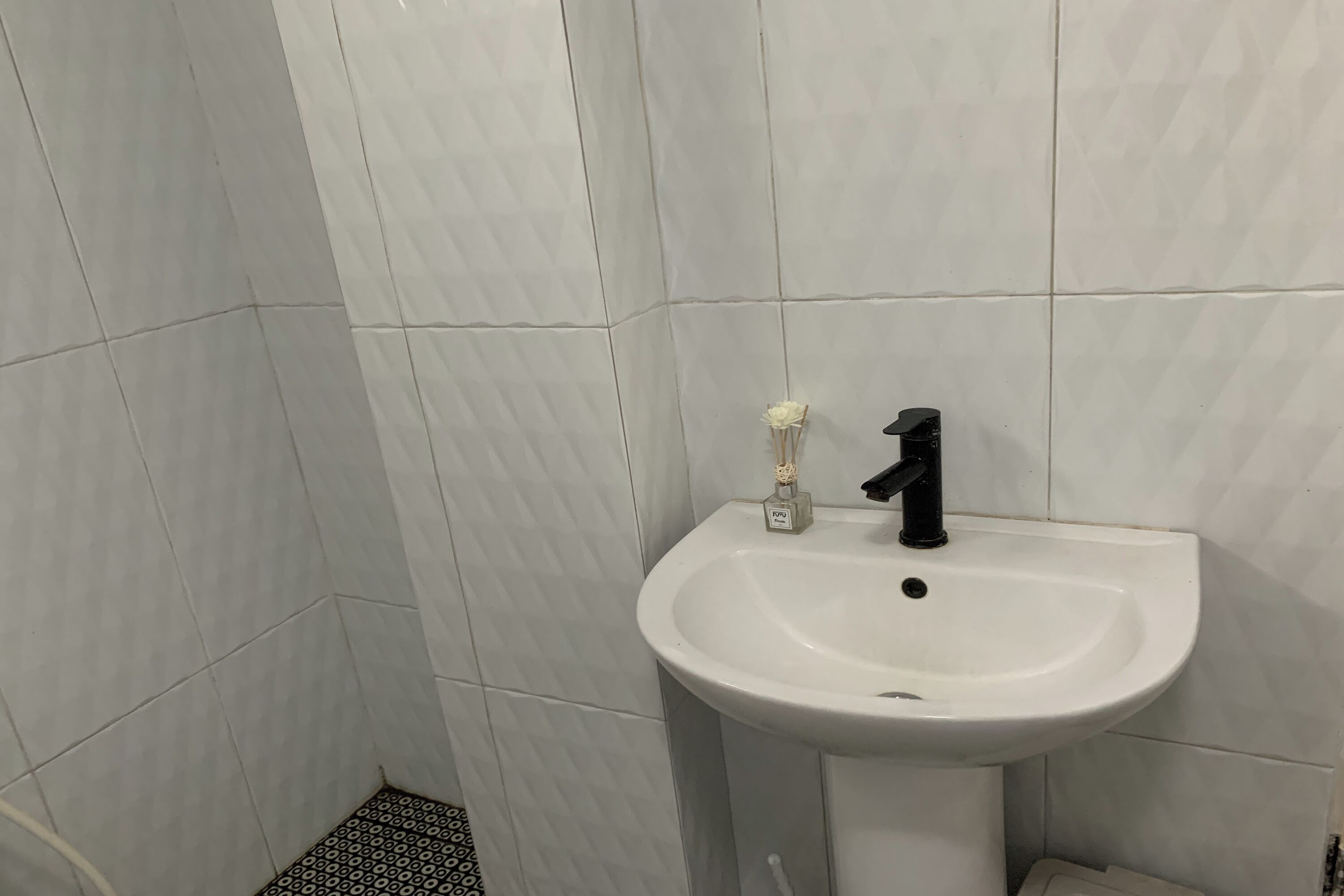 Casa de banho com azulejos brancos, lavatório branco, torneira preta e uma pequena embalagem de sabonete líquido.