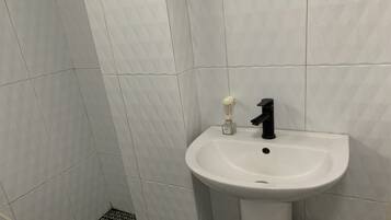 Casa de banho com azulejos brancos, lavatório branco, torneira preta e uma pequena embalagem de sabonete líquido.