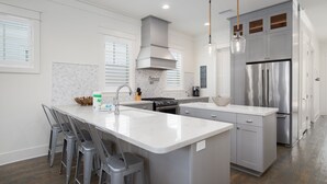 A modern kitchen with a central island, grey cabinetry, stainless steel appliances, and a herringbone tile backsplash.