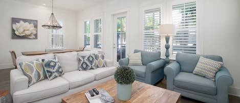 A living room with a light-colored sofa, two armchairs, a coffee table, and a potted plant.