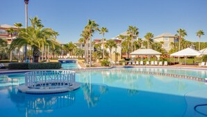 A swimming pool with lounge chairs, palm trees, and hotel buildings in the background.
