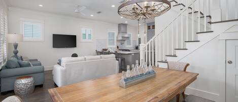 A modern living room with a wooden dining table, a grey sofa, and a chandelier.