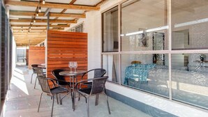 An outdoor seating area with a table and chairs, a wooden partition, and a view through large windows. - Prom Coast 1~Cosy beach life, stroll to the beach (Sandy Point)