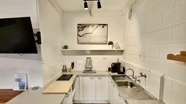 A modern kitchen with white cabinets, a central island, a built-in stove, and a hanging light fixture. - Prom Coast 1~Cosy beach life, stroll to the beach (Sandy Point)