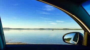 A car's side mirror reflecting a calm lake with a clear sky.