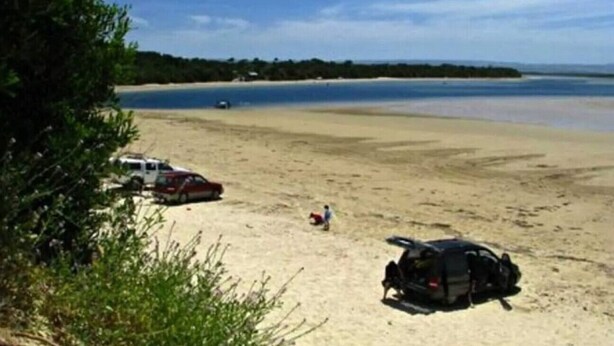 Ein Strand mit einem geparkten Fahrzeug und einem Rucksack im Sand.
