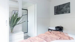 A bedroom with a bed, a bedside table, a black bag, a plant, and a shower area. - Prom Coast 1~Cosy beach life, stroll to the beach (Sandy Point)