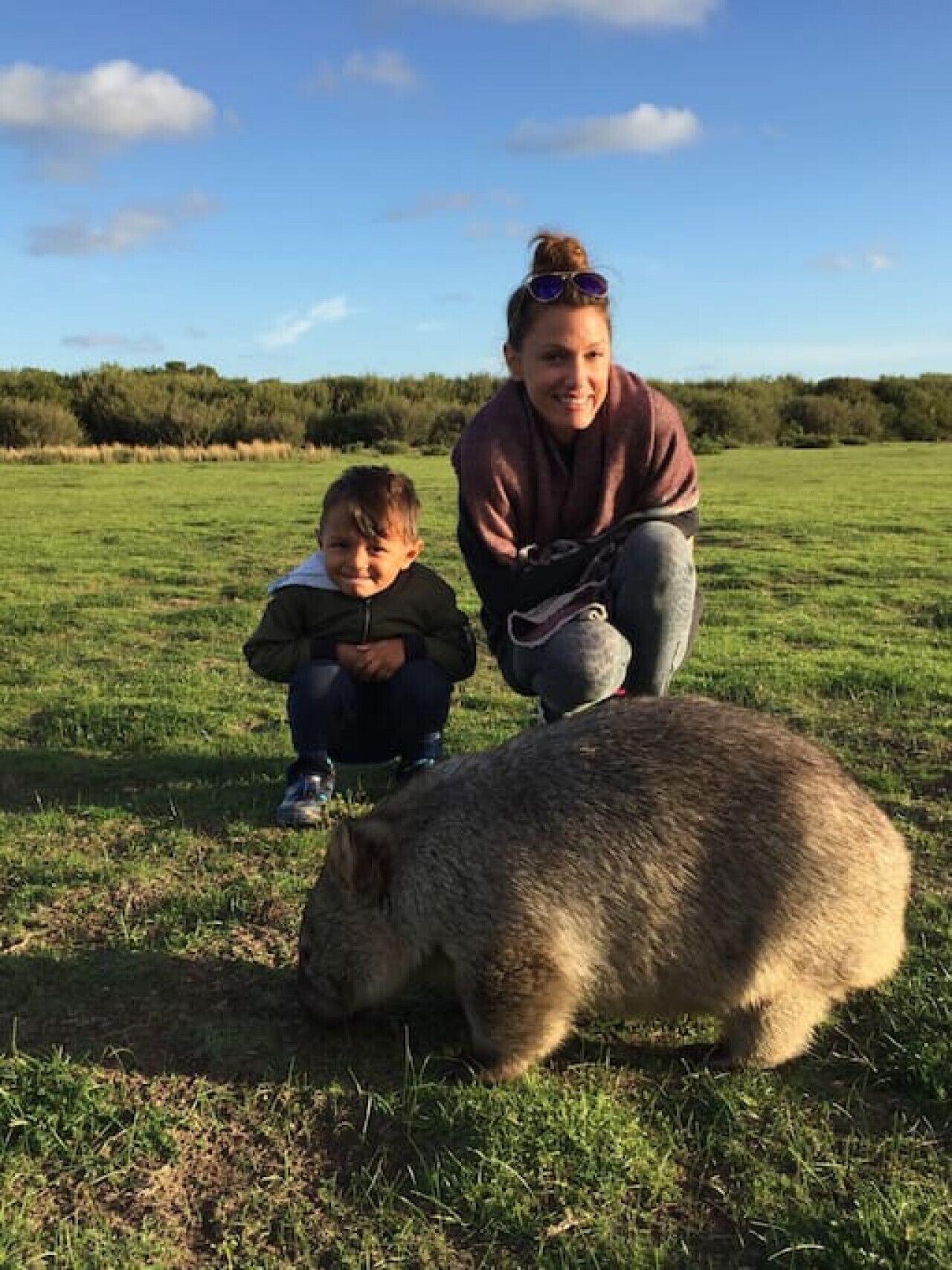 Une personne accroupie à côté d’un enfant et d’un grand animal dans un champ d’herbe.