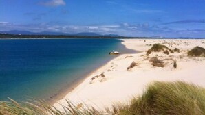 A beach with clear blue water, a sandy shore, and a boat. - Prom Coast 1~Cosy beach life, stroll to the beach (Sandy Point)