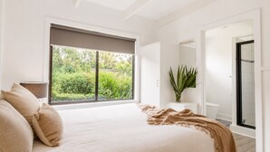 Ein Schlafzimmer mit großem Fenster, einem Bett, einem Nachttisch und einem Spiegel.