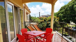 A balcony with a red table and chairs, a patterned curtain, and a view of greenery and buildings. - Case Latanier (Grand River South East)