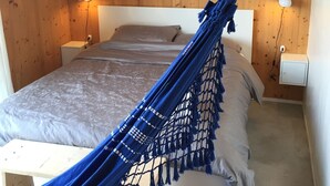 A bedroom with a hammock, wooden walls, a bed with a grey bedspread, two bedside lamps, and a painting on the wall. - Villino Nacci, in the heart of Tuscany. (San Miniato)