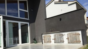 A modern building with large glass doors, a concrete patio, and a garage with wooden doors. - Villino Nacci, in the heart of Tuscany. (San Miniato)