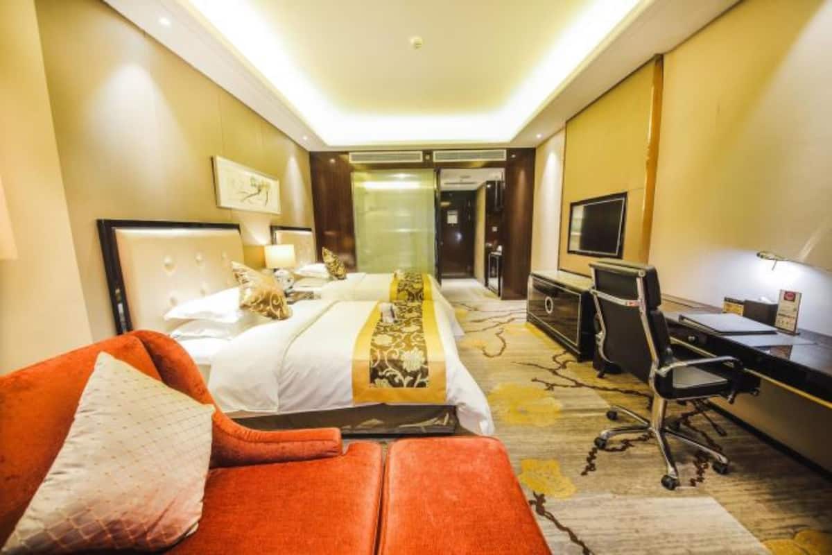 A hotel room with two beds, a desk, a chair, and a television.