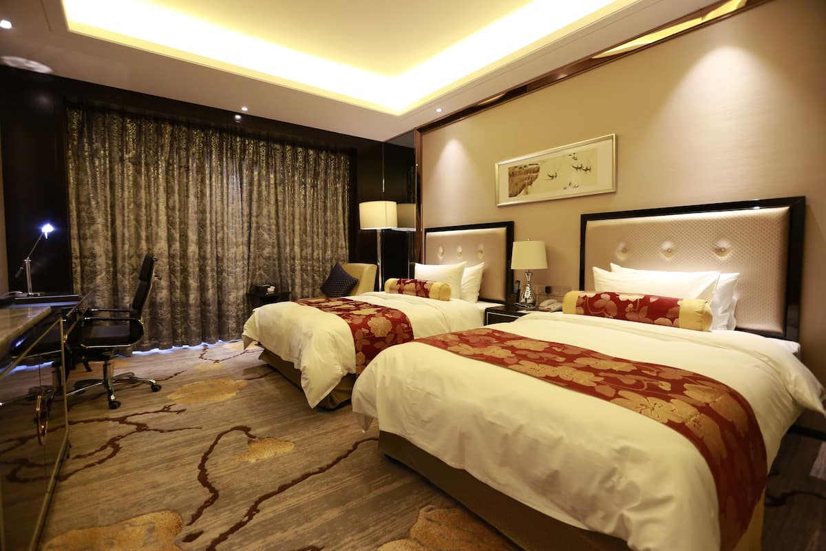 A hotel room with two beds, a desk, and a chair.