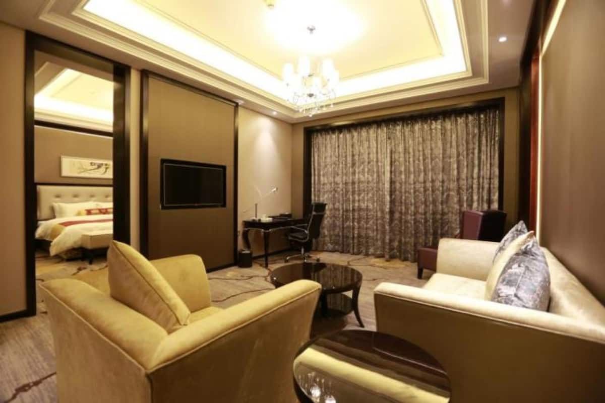 A hotel room with a bed, two sofas, a TV, a desk, and a chandelier.