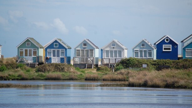 Une rangée de maisons de plage, avec une pelouse au premier plan et une étendue d’eau en arrière-plan.
