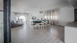 Una sala de estar moderna con comedor, que presenta una gran mesa de madera, sillas blancas y un sofá.