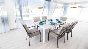 Un comedor con una mesa blanca dispuesta para seis personas, rodeada de sillas con asientos acolchados y patas oscuras.