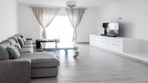 Una sala de estar moderna con un sofá gris, una mesa de centro y un televisor sobre un mueble blanco.