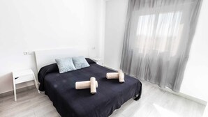 Habitación de hotel minimalista con cama, mesita de noche y un ventanal con cortinas translúcidas.