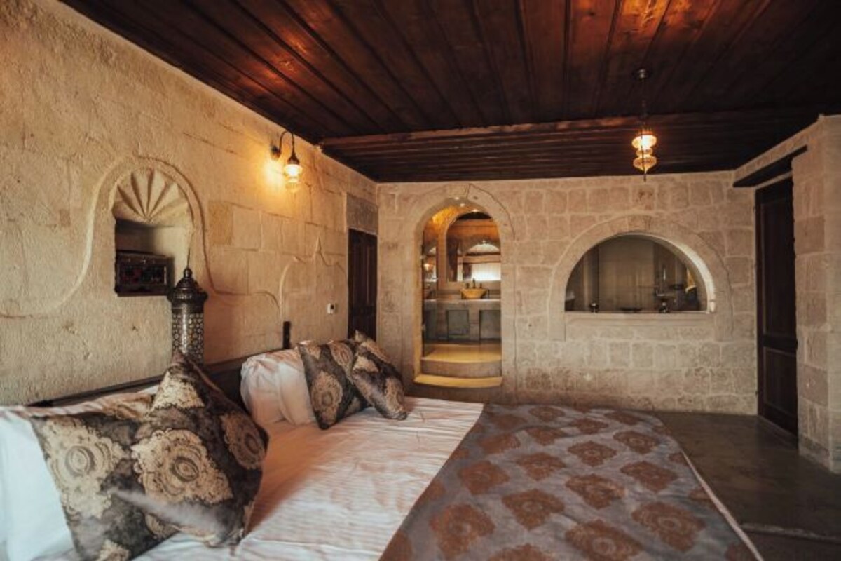 A room with a bed, stone walls, an arched doorway, and a fireplace.