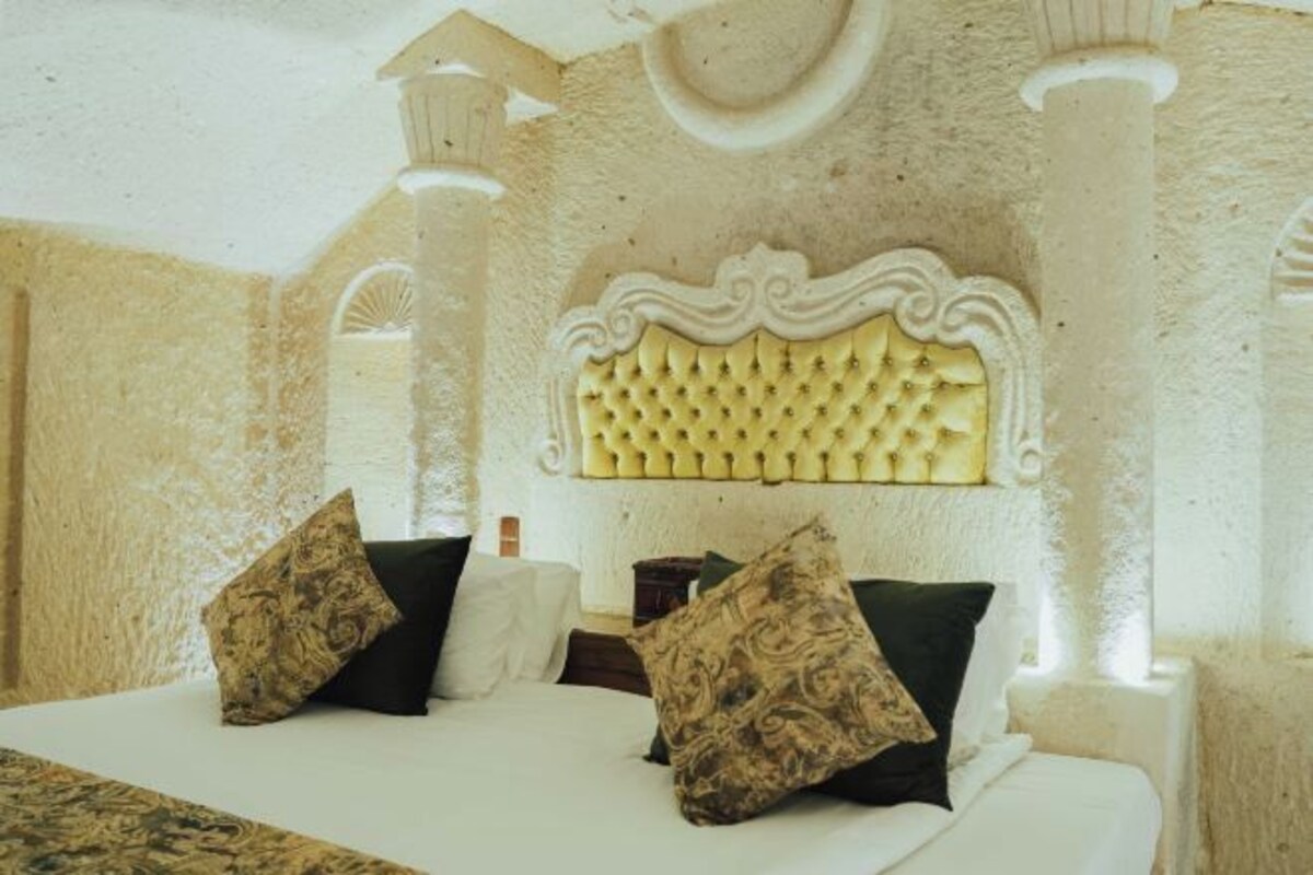 A bed with a tufted headboard, two pillows, and a white bedspread in a room with textured walls and columns.