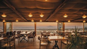 A restaurant with wooden tables and chairs, large windows offering a view of a mountain range. - Hu of Cappadocia (Nevsehir)