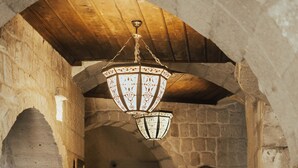 Passadís de parets de pedra amb sostre de fusta, llum penjant i una catifa amb disseny al terra.