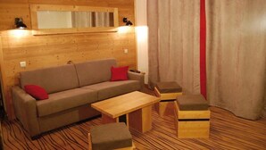 A cozy room with a wooden wall, a sofa with red cushions, a wooden coffee table, and two wooden ottomans. - Appart à 100m des Pistes | Accès piscine + Sauna! (Hauteluce)