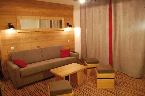 A cozy room with a wooden wall, a sofa with red cushions, a wooden coffee table, and two wooden ottomans.