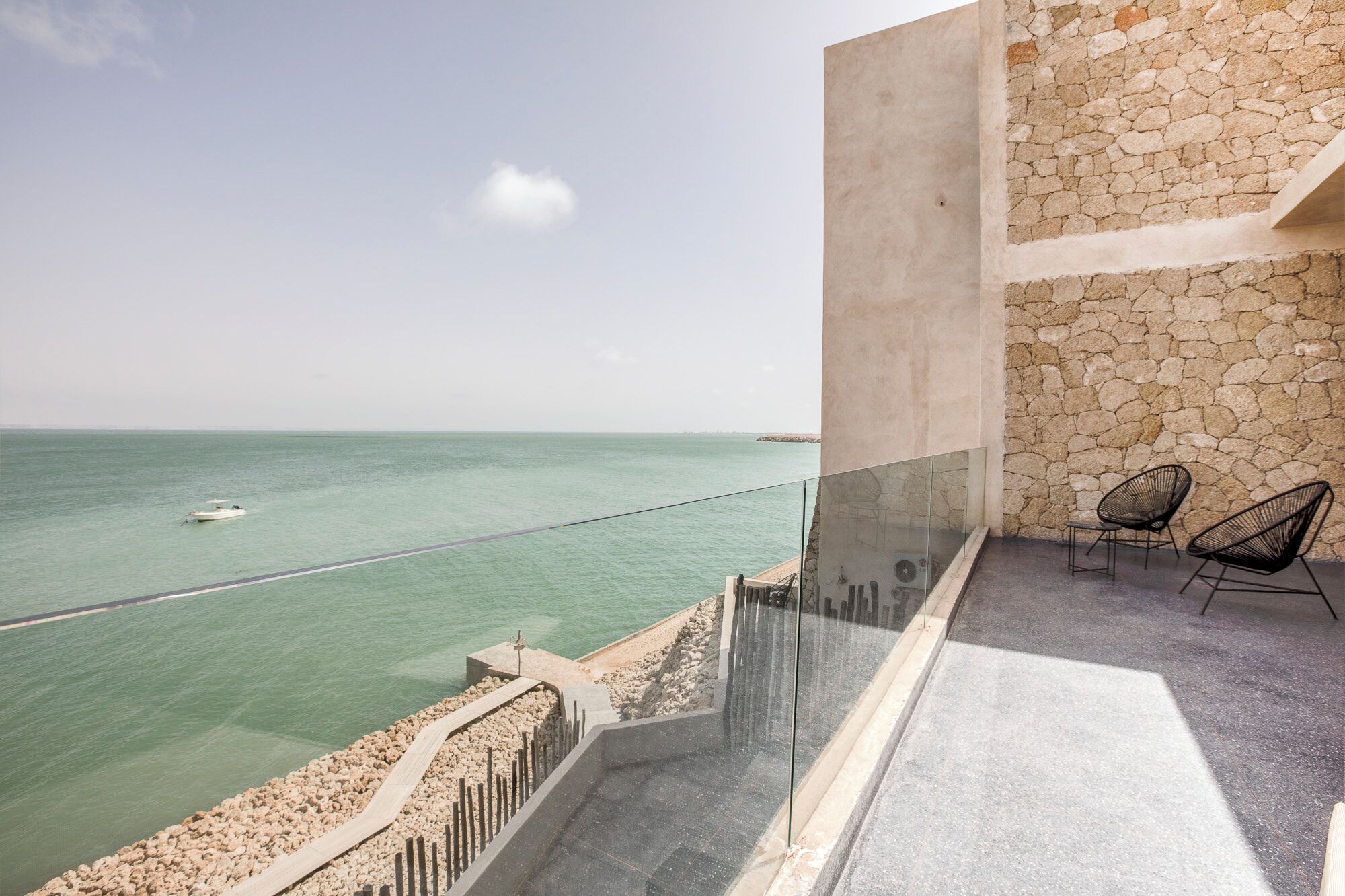 Ein Balkon mit Steinmauer, Glasgeländer und zwei schwarzen Stühlen.