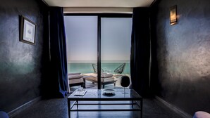 A room with a bed, a table, and two chairs, a framed picture on the wall, and a view of the sea through a large window. - Palais Rhoul Dakhla (Dakhla)