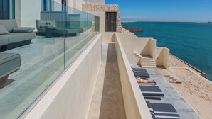 A modern outdoor lounge area with a glass balustrade, a stone pathway, and a seating area with cushions. - Palais Rhoul Dakhla (Dakhla)