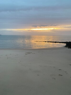 A beach with a calm sea, a rocky breakwater, and footprints in the sand.