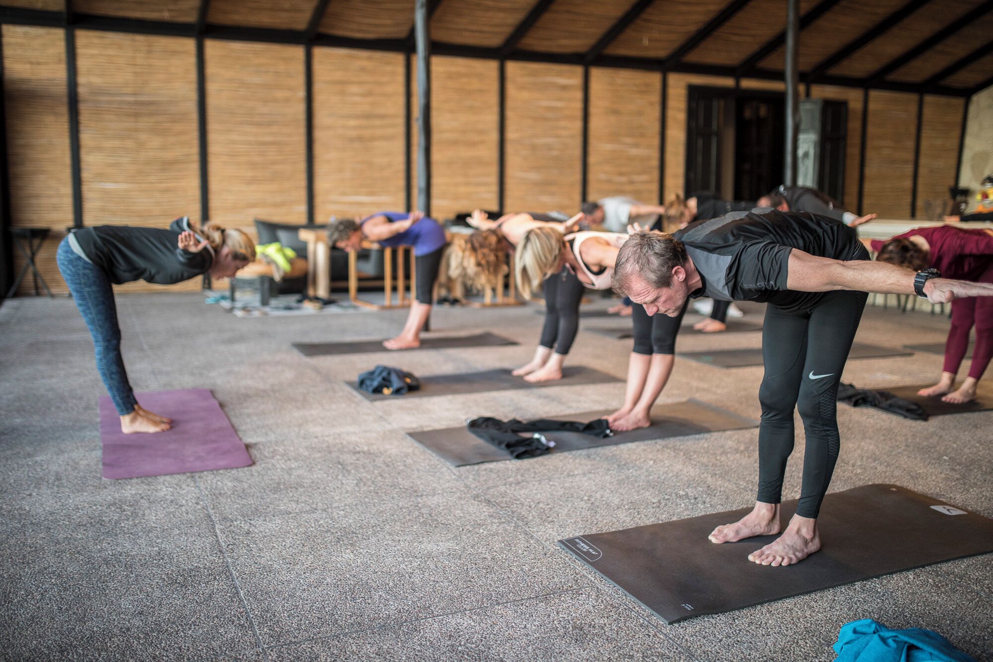 A group of people performing yoga in a spacious indoor area with wooden walls and a high ceiling.