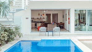 Una casa moderna con piscina, comedor y cocina visibles a través de puertas de cristal.