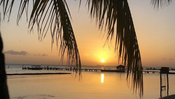 Escena de playa con un atardecer, agua tranquila y un muelle que se adentra en el mar.