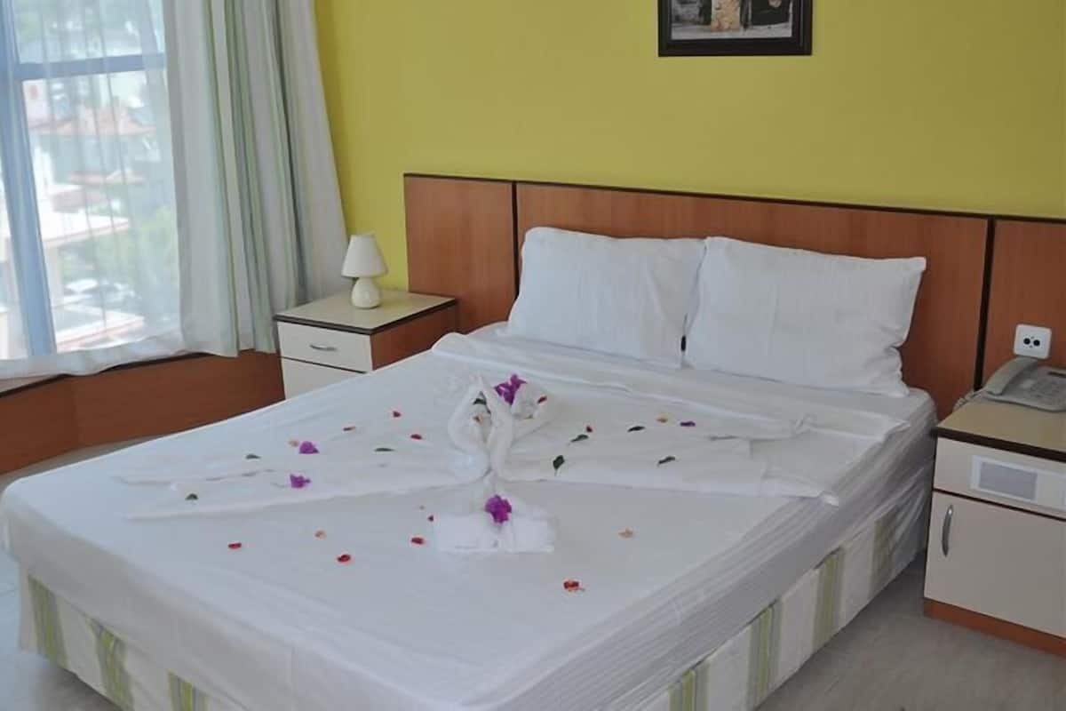Una habitación de hotel con cama, mesita de noche, lámpara y ventana con cortinas.