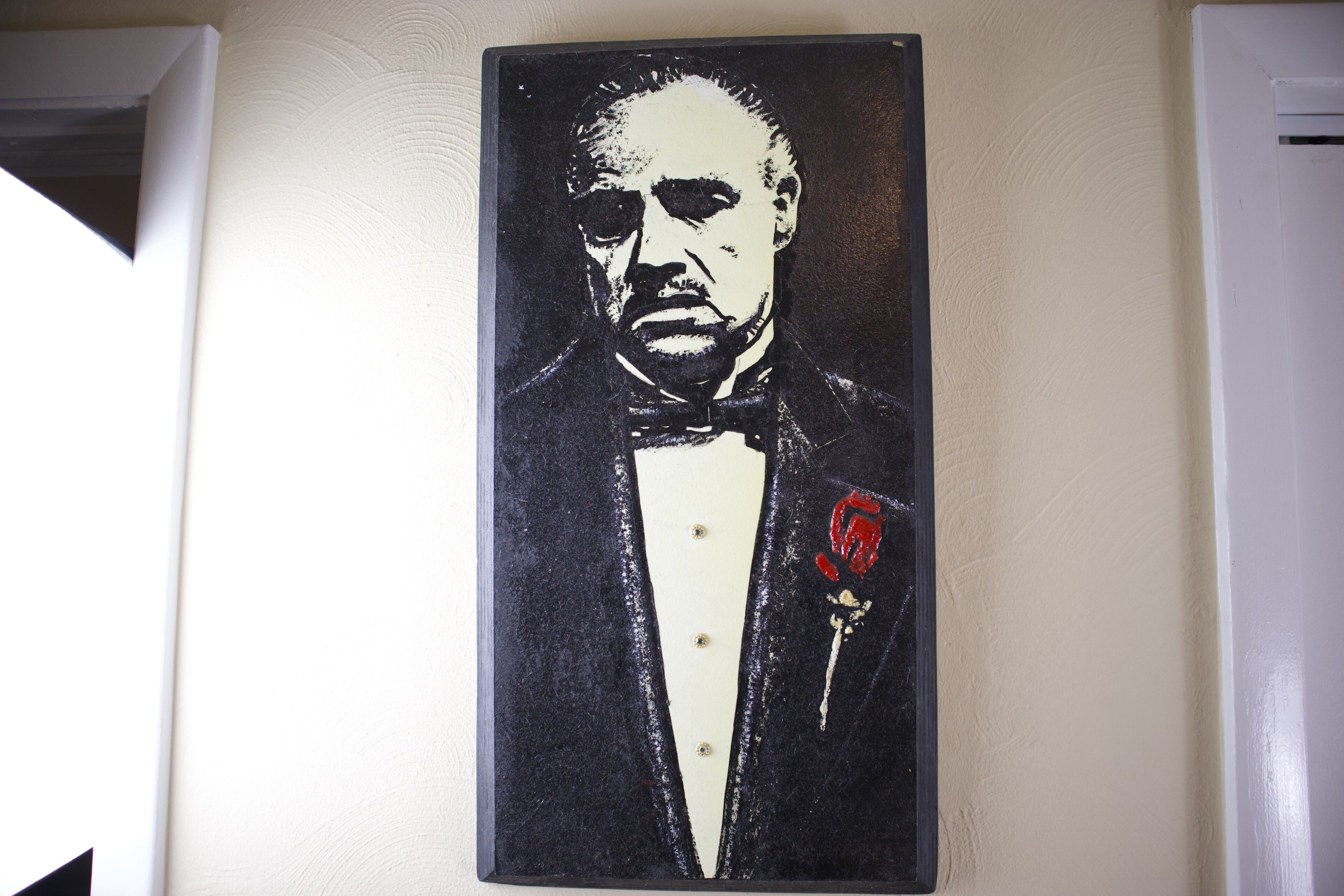 Un portrait d’un homme en smoking, portant une boutonnière avec une rose rouge, est accroché au mur.