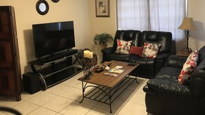Una sala de estar con televisor de pantalla plana, sofá de cuero, mesa de centro y ventilador de techo.